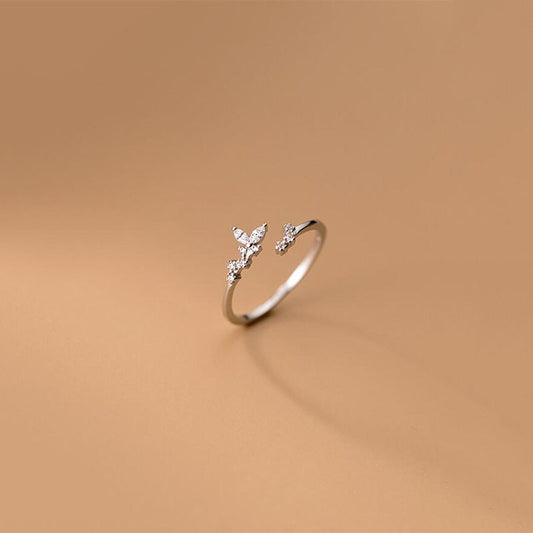 Silberner offener Ring mit Schmetterlingsdesign und Zirkonia-Steinen auf beigem Hintergrund.