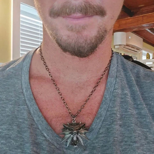 Mann mit grauem T-Shirt trägt silberne Hexer-Halskette, Wolf-Medaillon, Bart, Innenraum.