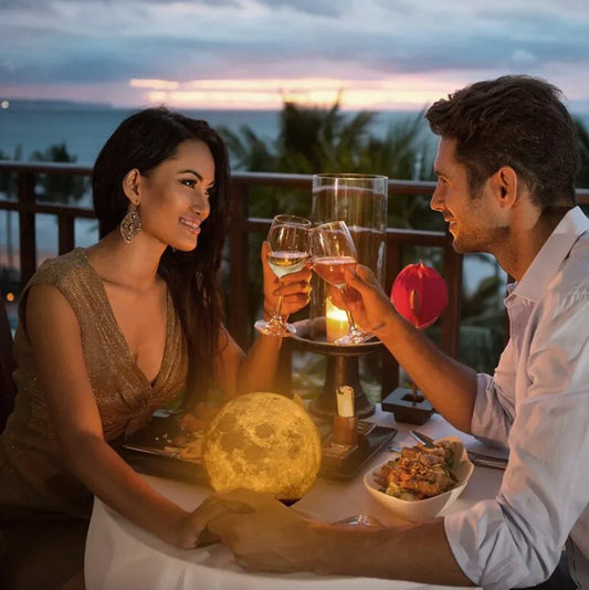 Paar beim romantischen Abendessen am Meer, Kerzenlicht, Sonnenuntergang, Weingläser, tropische Kulisse.