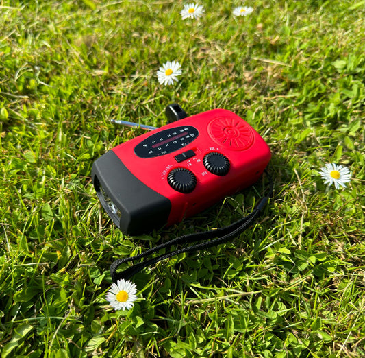 Rotes tragbares Notfallradio mit Solarpanel und Kurbel auf grünem Gras mit Gänseblümchen.