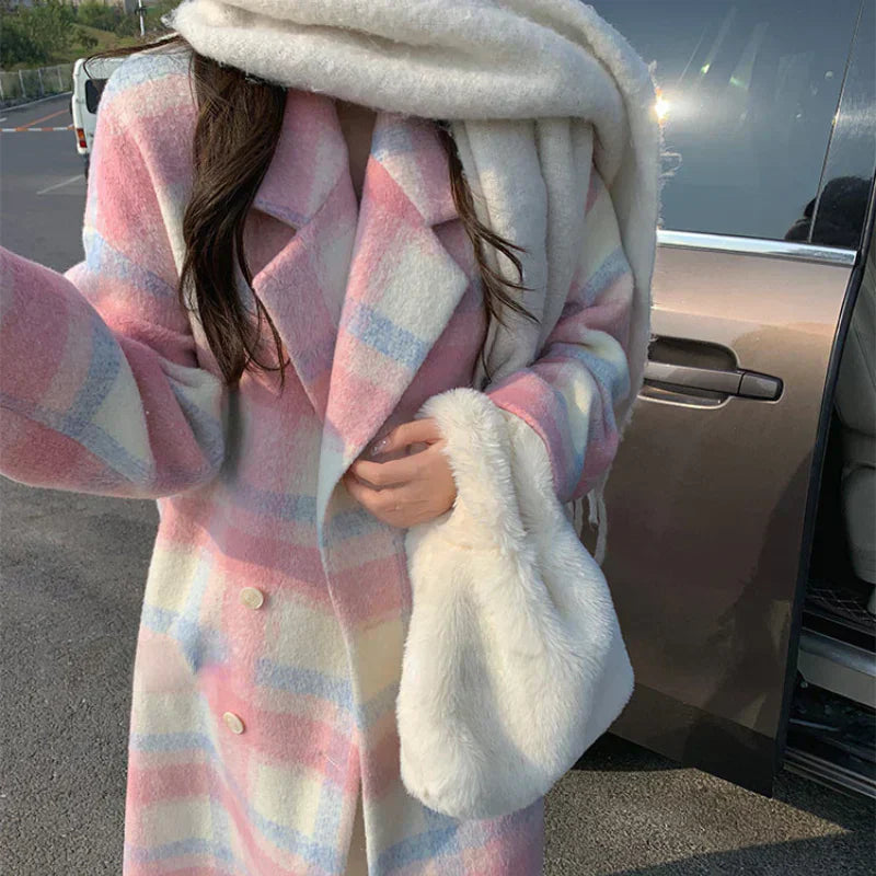 Frau im rosa karierten Mantel mit weißem Schal und Tasche, steht neben Auto.