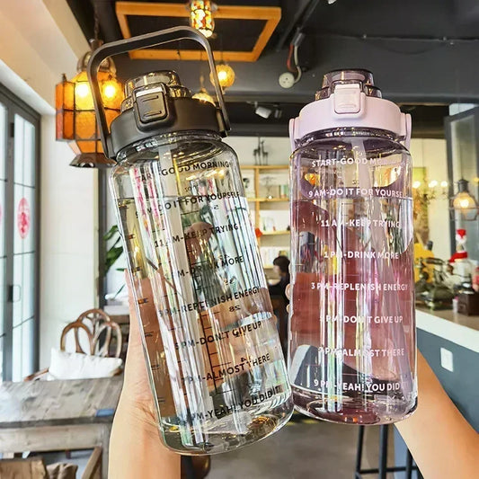 Zwei transparente Wasserflaschen mit Motivationsaufdruck, schwarz und rosa Deckel, im Café.