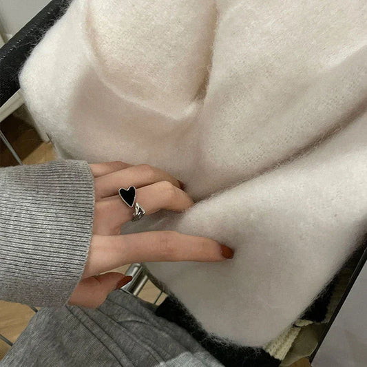 Damenhand mit Herzring berührt weiche, weiße Strickdecke aus Wolle im modernen Design.