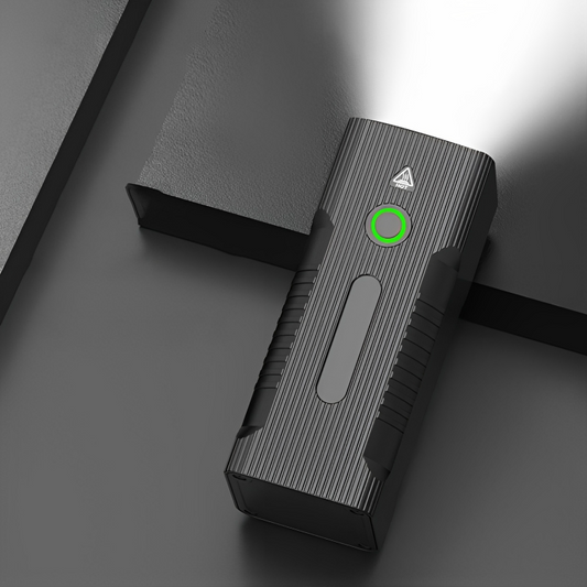 Schwarze LED-Taschenlampe, rechteckig, mit grünem Knopf, leuchtet auf dunklem Hintergrund.