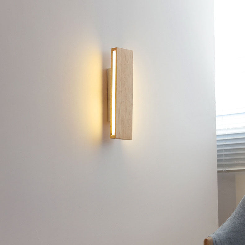 Rozsvícená svislá dřevěná lampa na bílé zdi u okna se žaluziemi, vedle šedé opěradlo křesla. 15