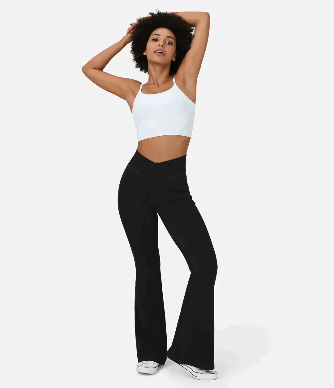 Frau in weißem Crop-Top und schwarzen Schlaghosen, modische Damenbekleidung, Studioaufnahme.