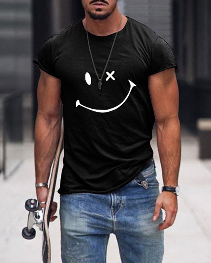 Mann in schwarzem T-Shirt mit Smiley-Design, Jeans, Skateboard, urbaner Hintergrund.