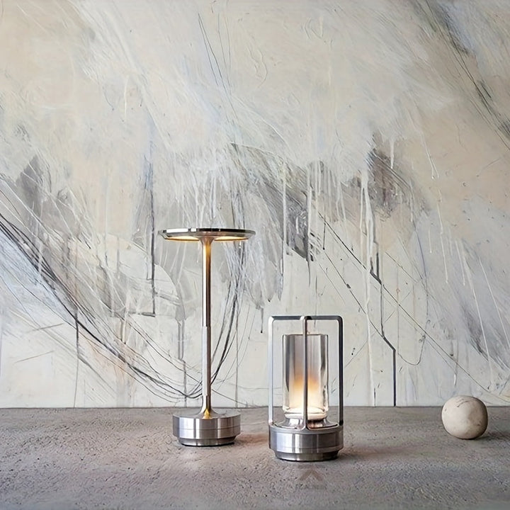 Moderne Tischlampen aus Metall, minimalistisch, silberfarben, auf Betonoberfläche vor abstrakter Wand.