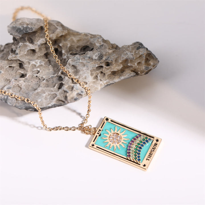 Goldene Halskette mit Tarot-Anhänger, Sonnenmotiv, türkisfarben, auf grauem Stein.