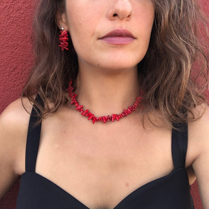 Frau mit roter Korallenkette und passenden Ohrringen vor rotem Hintergrund.