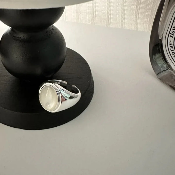 Silberner Siegelring mit weißem Stein auf schwarzem Tisch, elegantes Schmuckdesign.