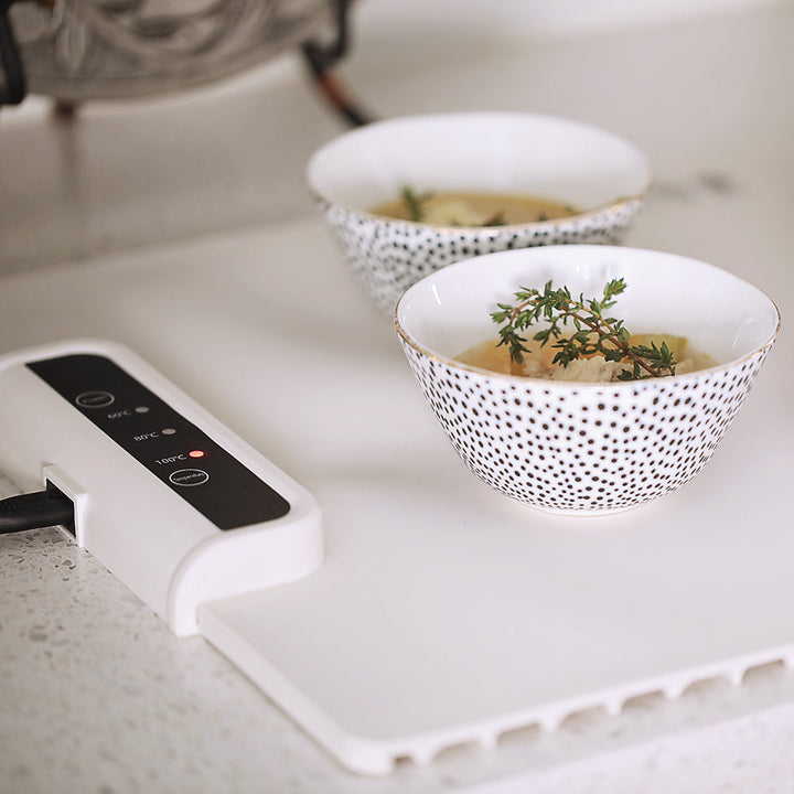 Zwei Schalen mit Suppe auf weißem Tisch, dekoriert mit Thymian, neben digitalem Heizgerät.