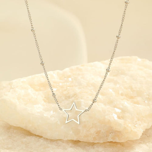 Silberne Stern-Halskette auf hellem Stein, eleganter Schmuck, minimalistisches Design.