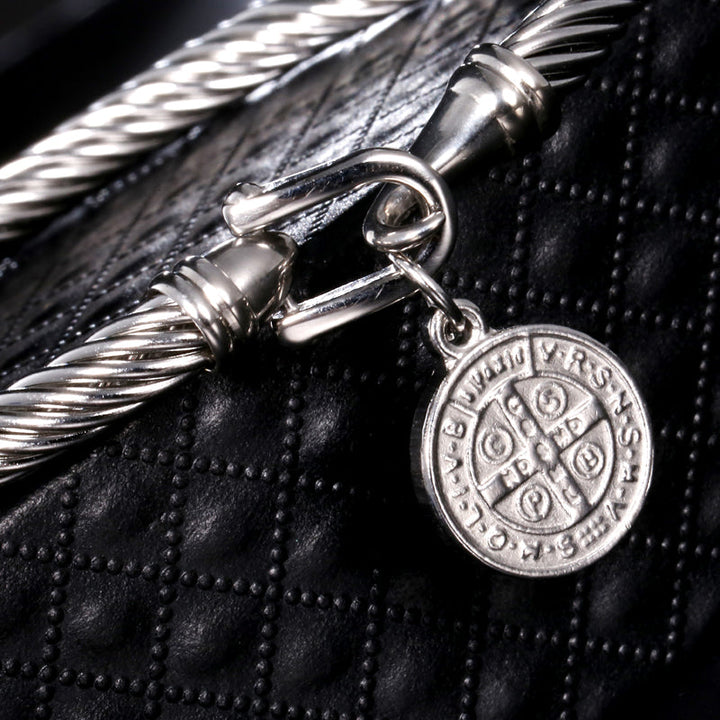 Silberarmband mit rundem Anhänger, geflochtenes Design, auf schwarzem Lederhintergrund.