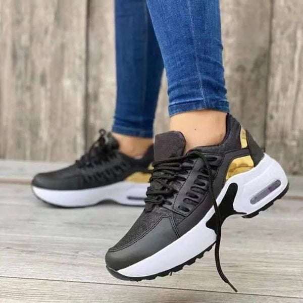 Schwarze Damen-Sneaker mit goldenen Akzenten, weiße Sohle, lässige Mode, Holzboden.