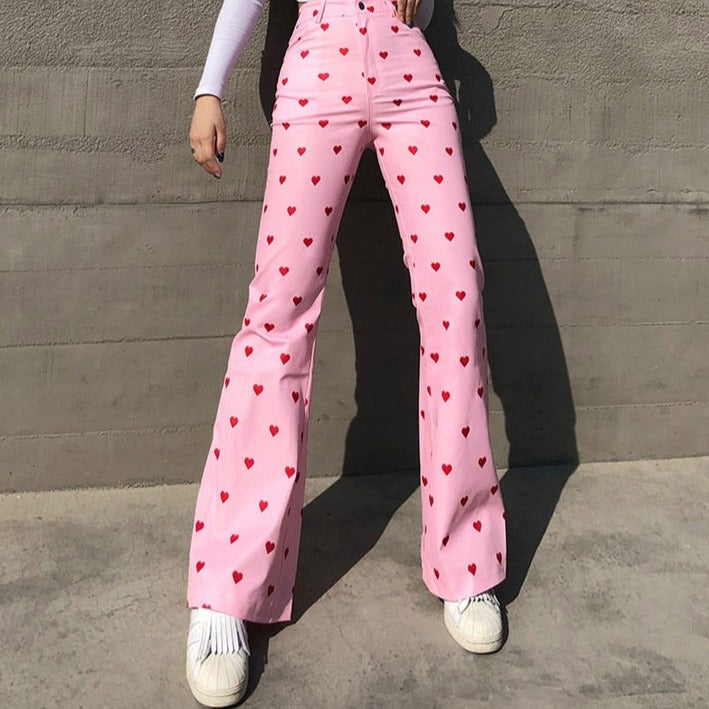 Frau in rosa Schlaghose mit roten Herzen, weiße Sneaker, modische Damenbekleidung.