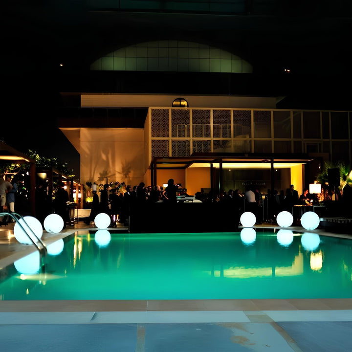 Beleuchteter Pool bei Nacht mit modernen Kugelleuchten und stilvoller Architektur im Hintergrund.