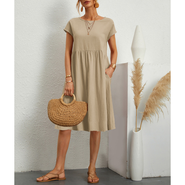 Frau in beige Baumwoll-Leinen-Kleid, Boho-Stil, mit Strohtasche und Sandalen.