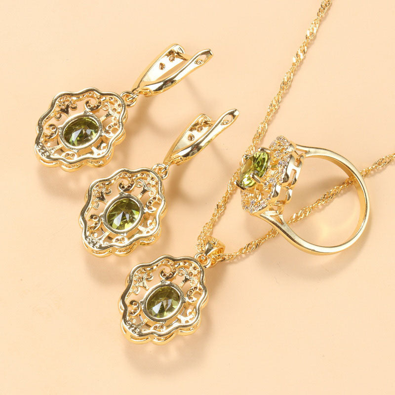 Goldene Schmuckset mit olivgrünen Zirkonia, bestehend aus Ohrringen, Ring und Halskette.