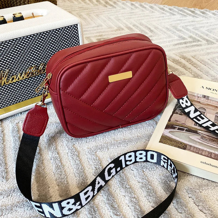 Rote Umhängetasche aus Leder mit gestepptem Design und verstellbarem Schultergurt.