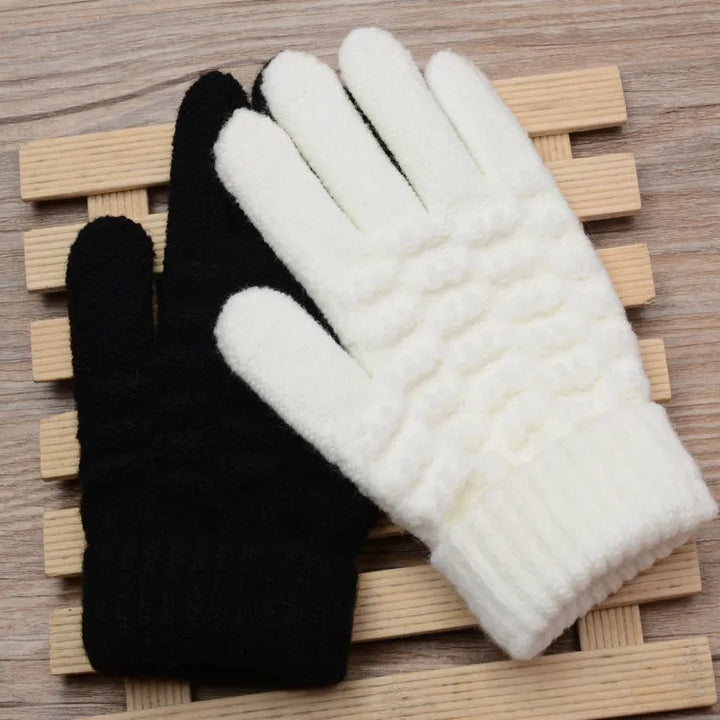 Schwarze und weiße Strickhandschuhe aus Wolle auf Holzunterlage, Wintermode Accessoire.