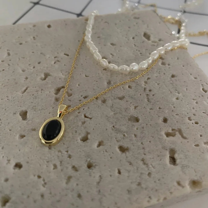 Goldene Halskette mit schwarzem Anhänger und Perlenkette auf Steinuntergrund.