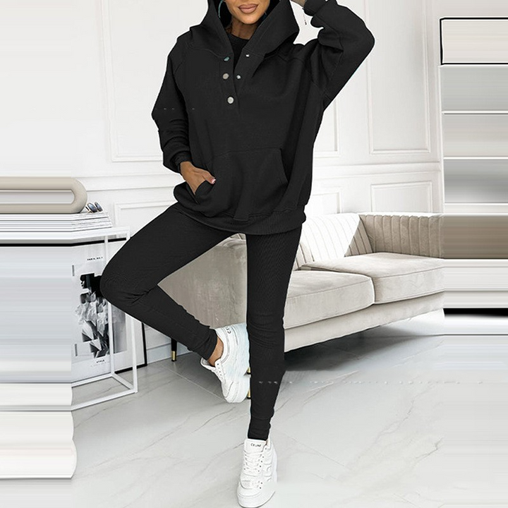 Frau in schwarzem Hoodie und Leggings, weiße Sneaker, modernes Wohnzimmer, Freizeitmode.