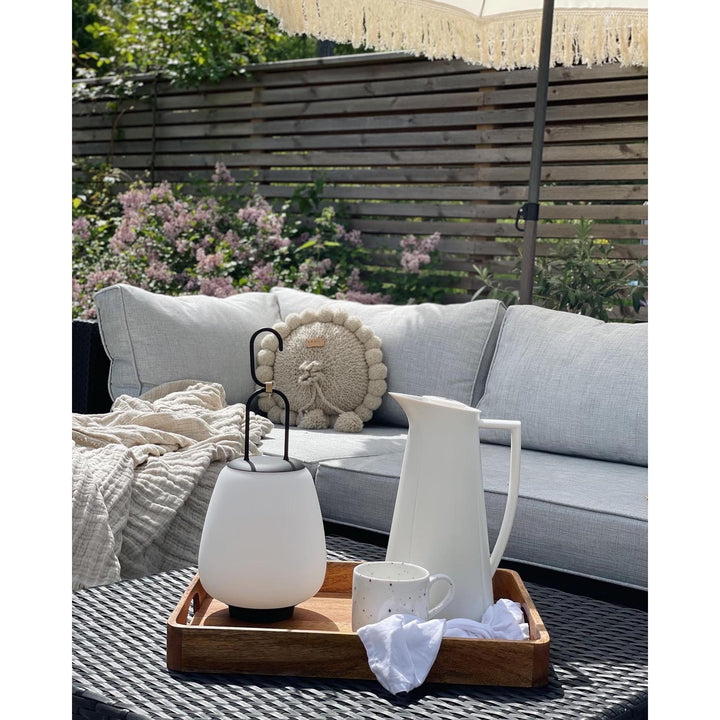 Weiße LED-Laterne und Kanne auf Holztablett, Gartenmöbel, Outdoor-Dekoration, Sommer.