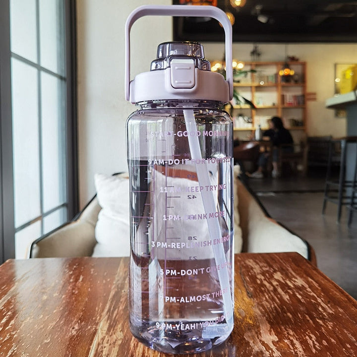Transparente Wasserflasche mit Zeitmarkierungen, lila Deckel, auf Holztisch im Café.