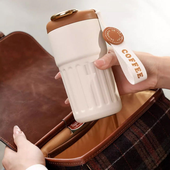 Beiger Thermobecher mit braunem Deckel und COFFEE-Schriftzug, ideal für unterwegs.