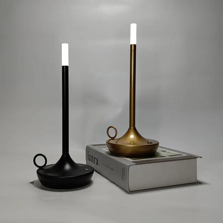 Zwei moderne LED-Kerzenleuchter, schwarz und gold, auf einem Buch, minimalistisches Design.