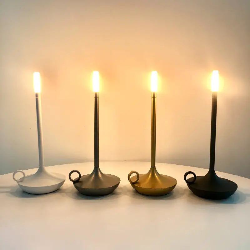 Vier moderne LED-Kerzenleuchter in Weiß, Grau, Gold und Schwarz auf einem Tisch.