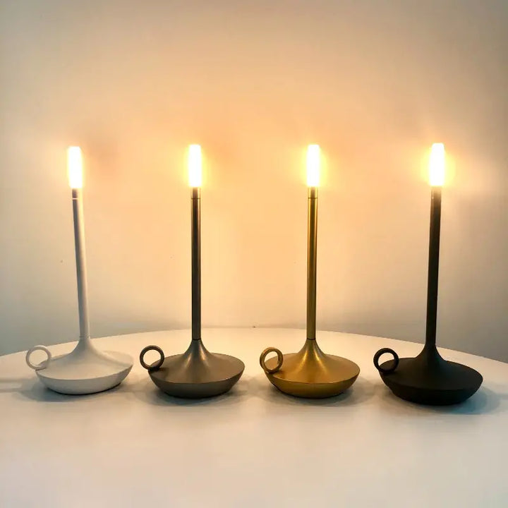 Vier moderne LED-Kerzenleuchter in Weiß, Grau, Gold und Schwarz auf einem Tisch.