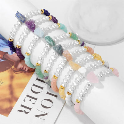 Armbänder mit weißen Perlen, bunten Edelsteinen und goldenen Akzenten auf Marmortisch.