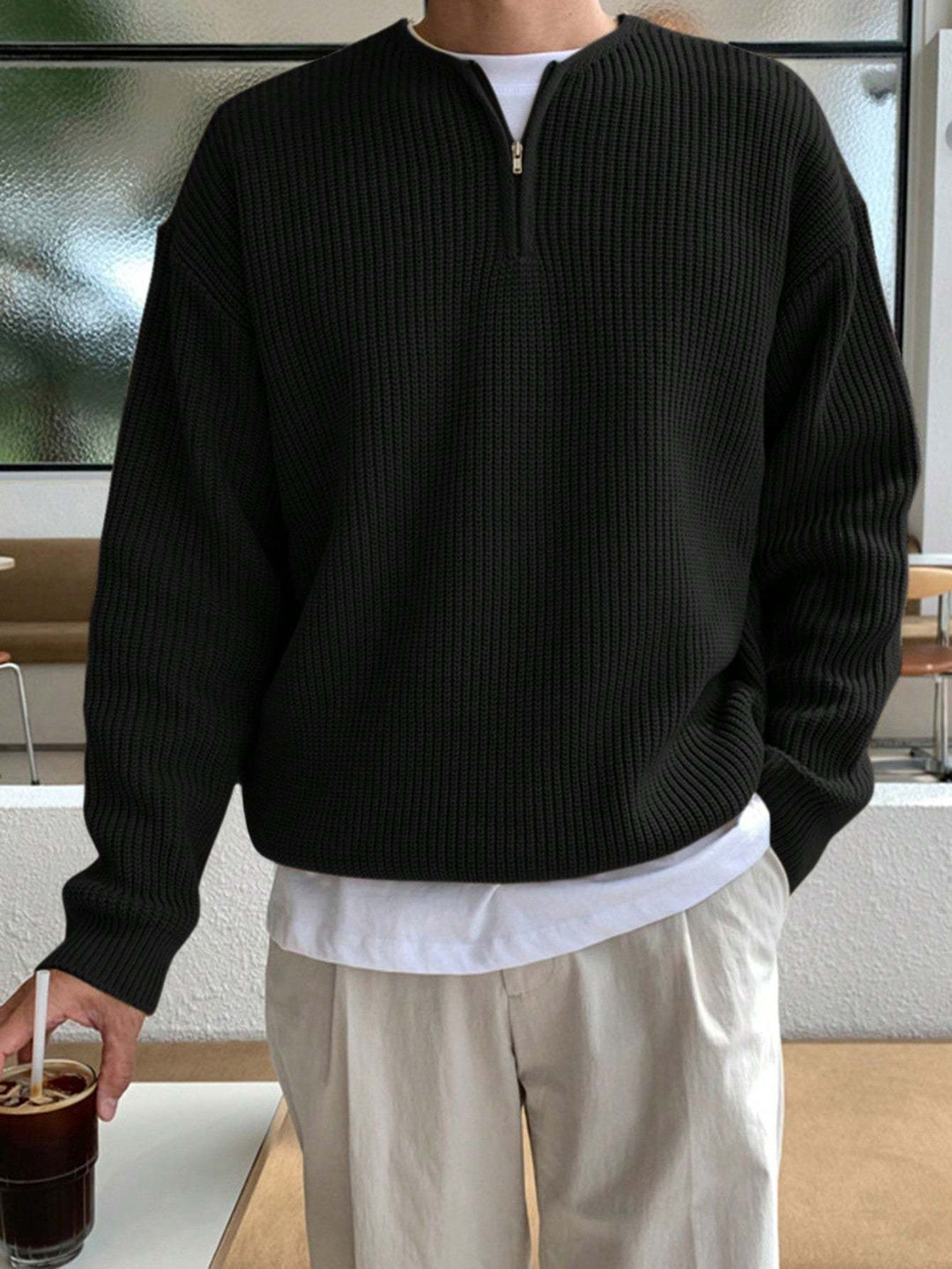 Mann in schwarzem Strickpullover mit Reißverschluss, hält ein Glas Eiskaffee, lässige Mode.