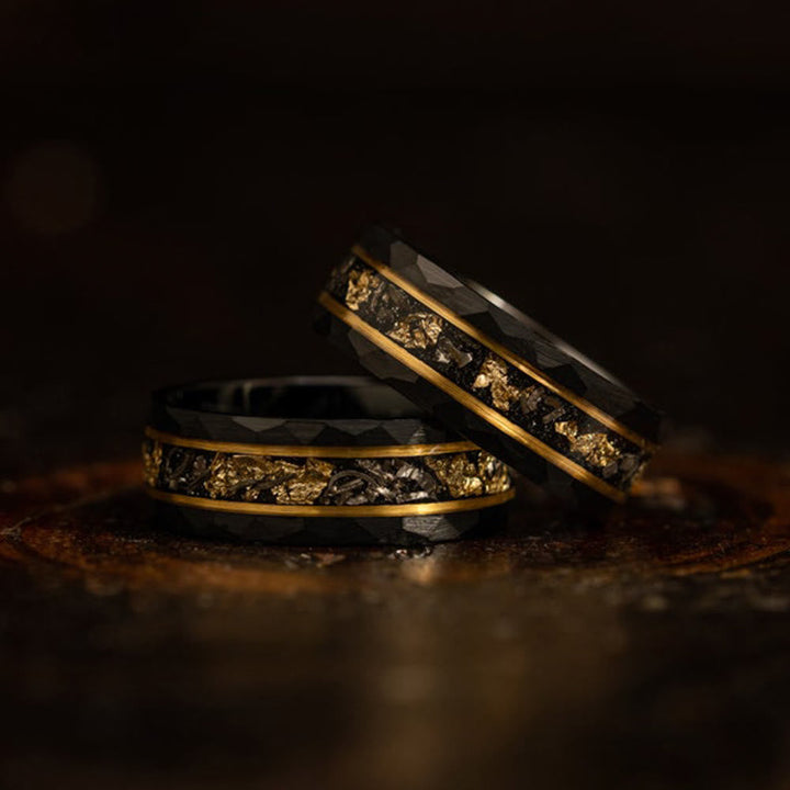 Zwei schwarze Wolframringe mit goldenen Akzenten und facettiertem Design auf dunklem Hintergrund.