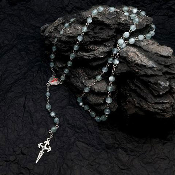Silberne Rosenkranzkette mit grünen Perlen und Kreuzanhänger auf schwarzem Hintergrund.