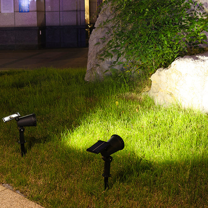 Schwarze Solar-Gartenleuchten beleuchten Rasen vor Stein und Pflanzen bei Nacht.