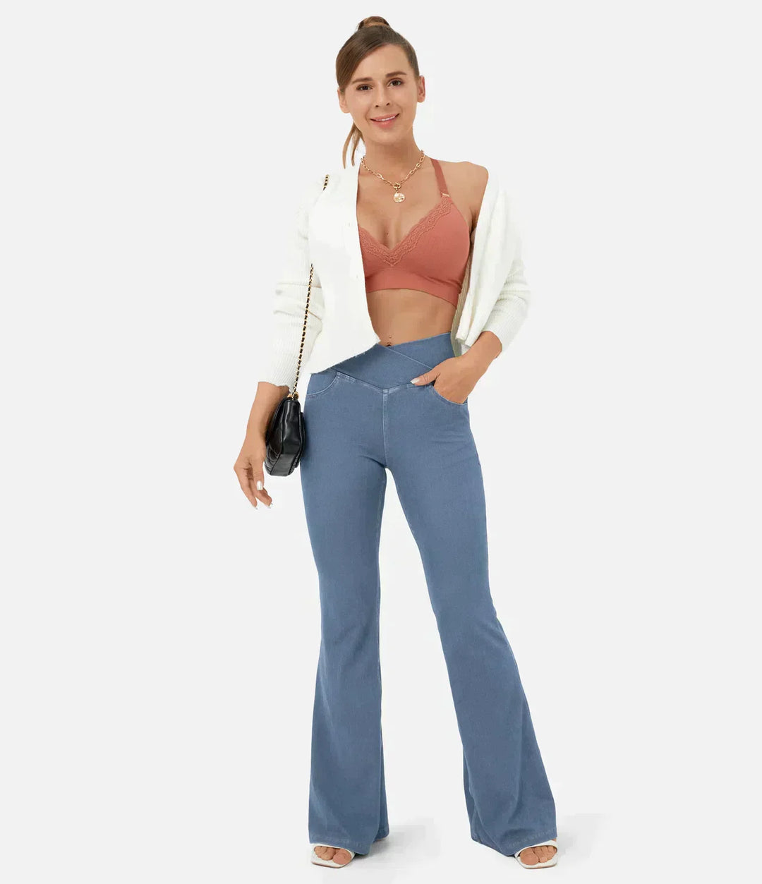 Frau in blauer Schlaghose, weißem Blazer, rotem Top, mit schwarzer Tasche, modisch gekleidet.
