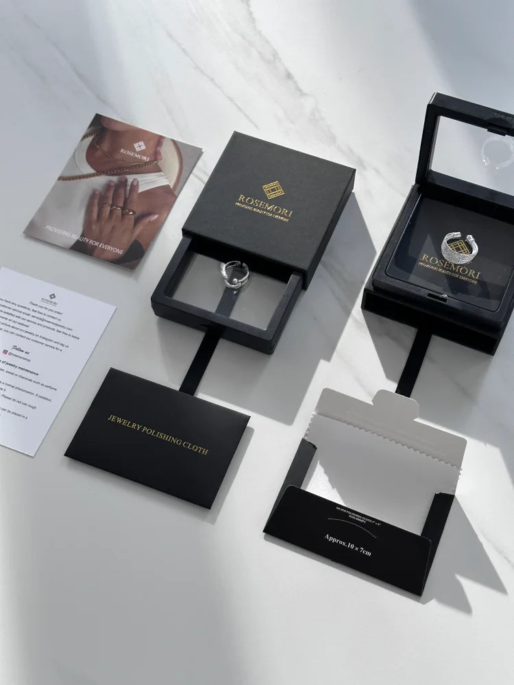 Schwarze Schmuckschachteln mit Ring, Rosimori-Logo, Schmuckpoliertuch, auf weißem Hintergrund.