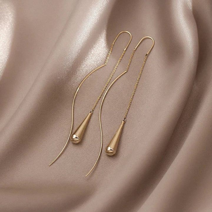 Goldene Ohrringe auf beigem Seidenstoff, minimalistisches Design, eleganter Schmuck.