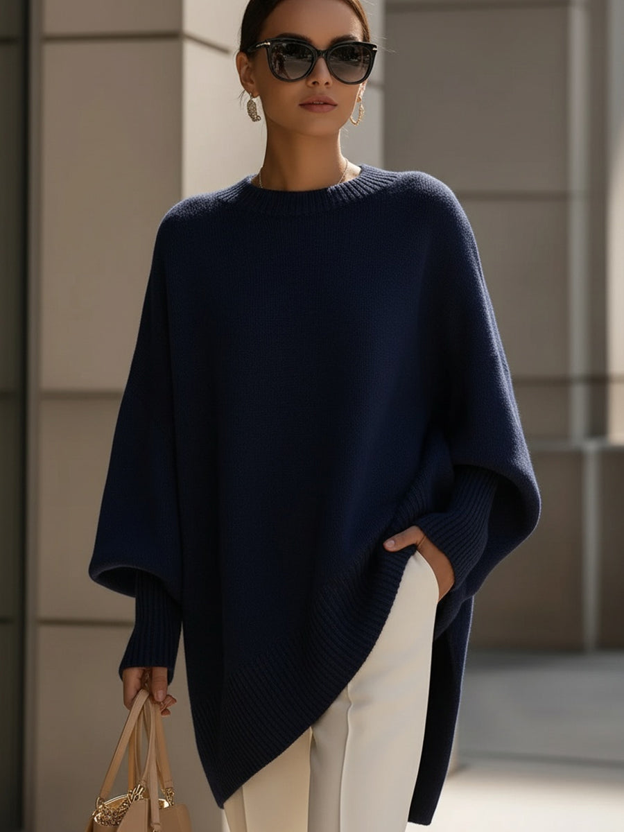 Tmavě modré pletené pončo na modelce se slunečními brýlemi, kombinované s bílými kalhotami 9