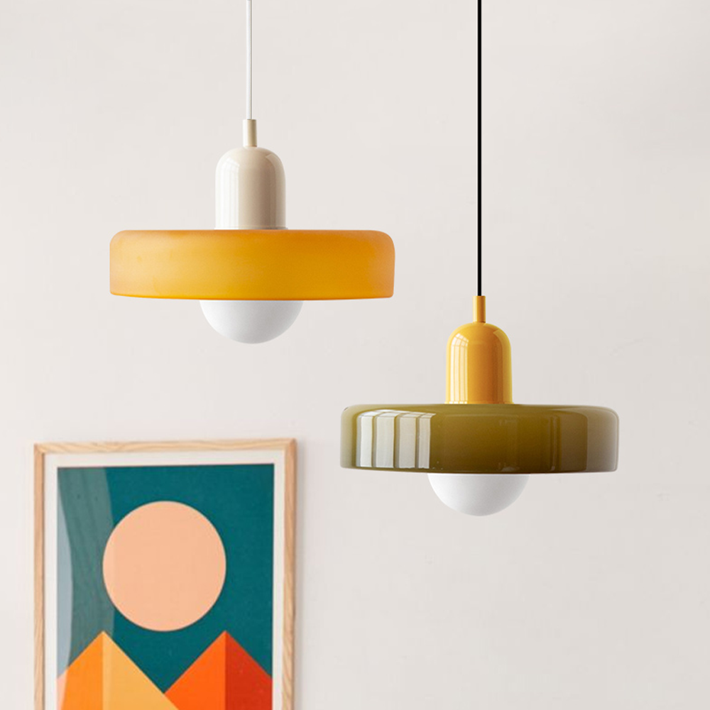 Zwei moderne Pendelleuchten, gelb und olivgrün, aus Glas, vor minimalistischem Kunstwerk.