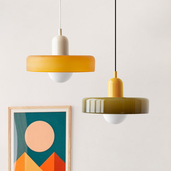 Zwei moderne Pendelleuchten, gelb und olivgrün, aus Glas, vor minimalistischem Kunstwerk.