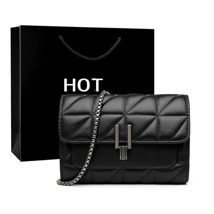 Schwarze Lederhandtasche mit Kettengurt vor schwarzer Geschenktüte, elegant und modern.