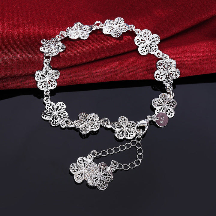 Silbernes Armband mit filigranen Blumenanhängern auf rotem Stoffhintergrund.
