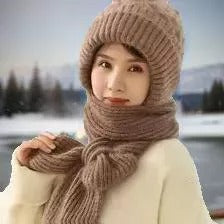Frau mit brauner Strickmütze und Schal im Winter, vor schneebedeckter Landschaft.