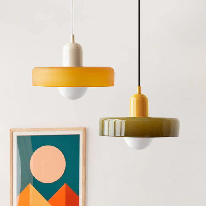 Zwei moderne Hängelampen, gelb und olivgrün, aus Glas, vor abstraktem Kunstwerk.