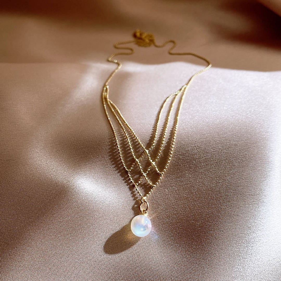 Goldene Halskette mit Perlenanhänger auf Seidenstoff, eleganter Schmuck, Damenaccessoire.