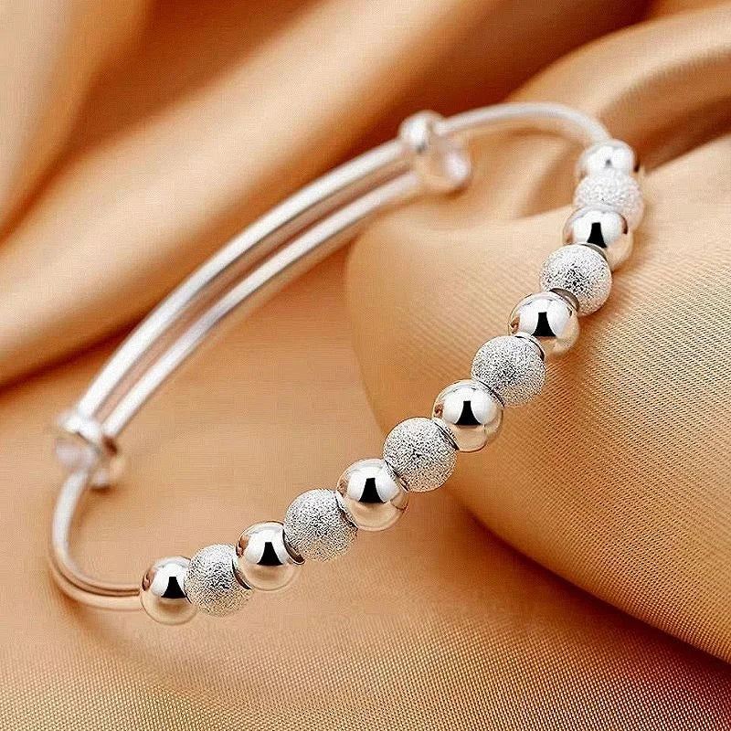 Silberarmband mit glänzenden und matten Kugeln auf goldenem Stoffhintergrund.